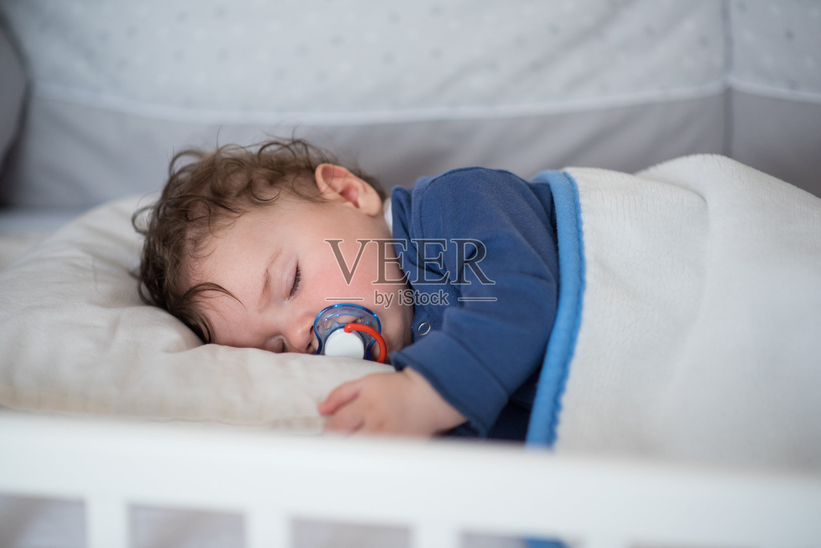 家庭时刻，小男孩睡在他的婴儿床里照片摄影图片