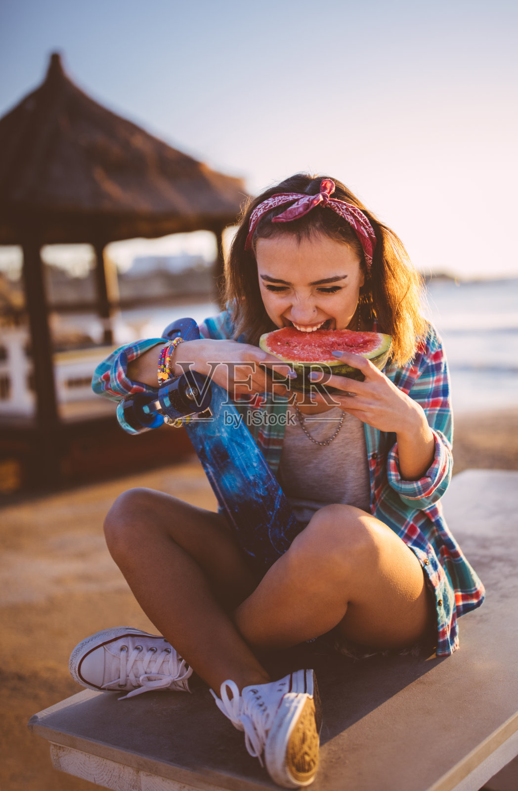 年轻漂亮的女孩玩滑板在海滩上吃西瓜照片摄影图片
