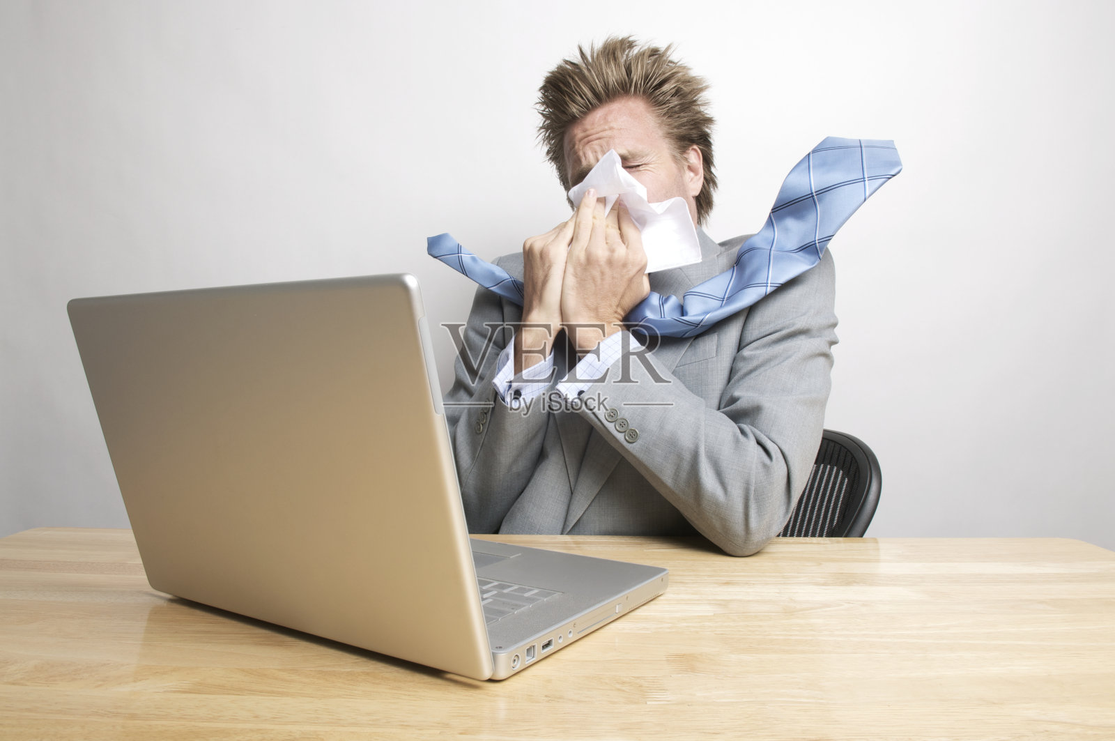 一个生病的商人坐在办公桌前擤鼻涕照片摄影图片