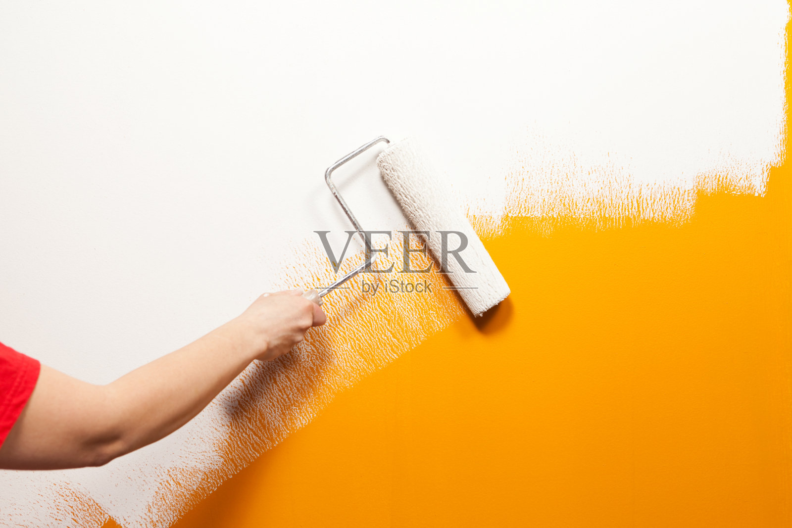 油漆工在旧橘色墙壁上滚动白色油漆照片摄影图片