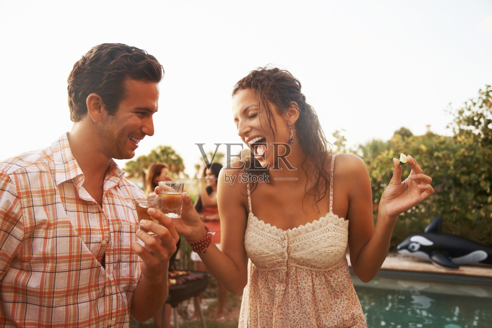 一对夫妇喝着龙舌兰酒，他们的朋友在后面照片摄影图片