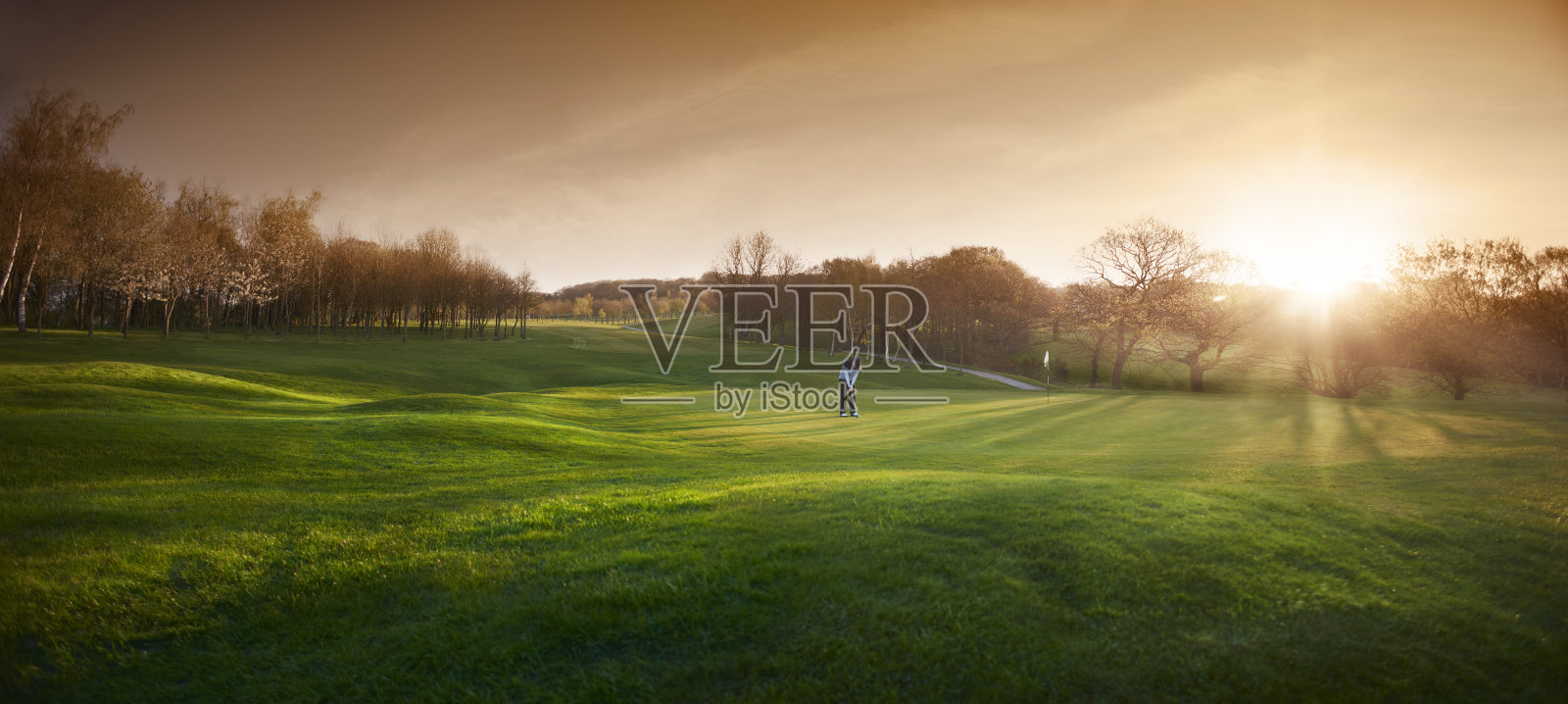 背光高尔夫球场与高尔夫球手在一个果岭照片摄影图片