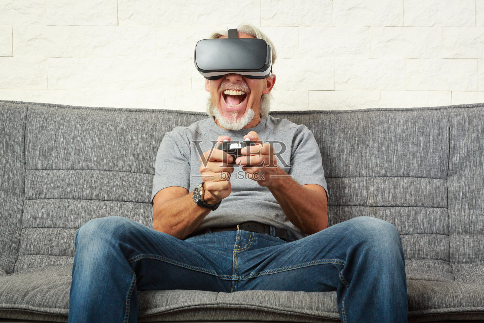 老男人坐在沙发上，玩虚拟现实游戏照片摄影图片
