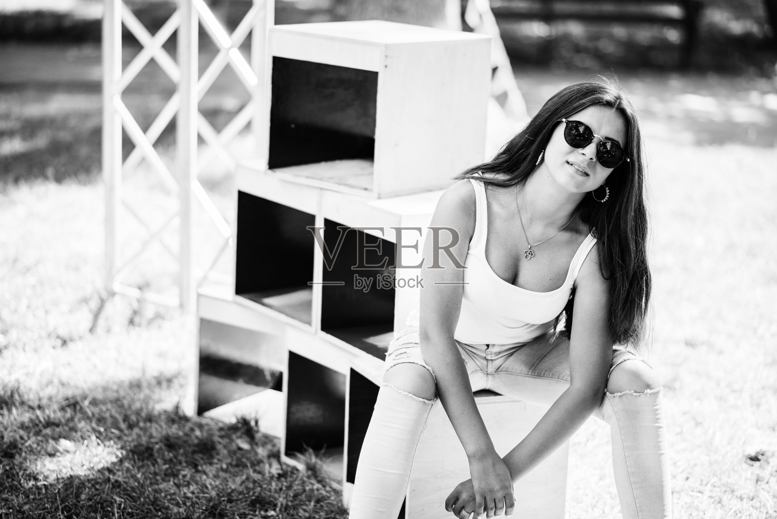 一个阳光明媚的日子里，一个穿着时尚的女孩在公园的木箱上摆姿势。黑白照片。照片摄影图片