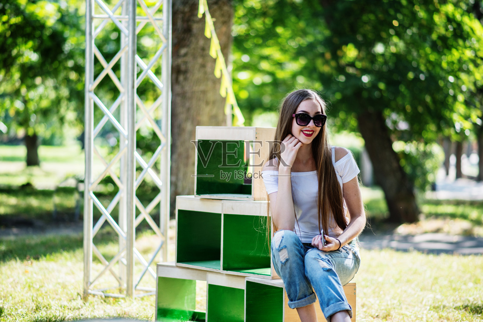 一个阳光明媚的日子里，一个穿着时尚的女孩在公园的木箱上摆姿势照片摄影图片