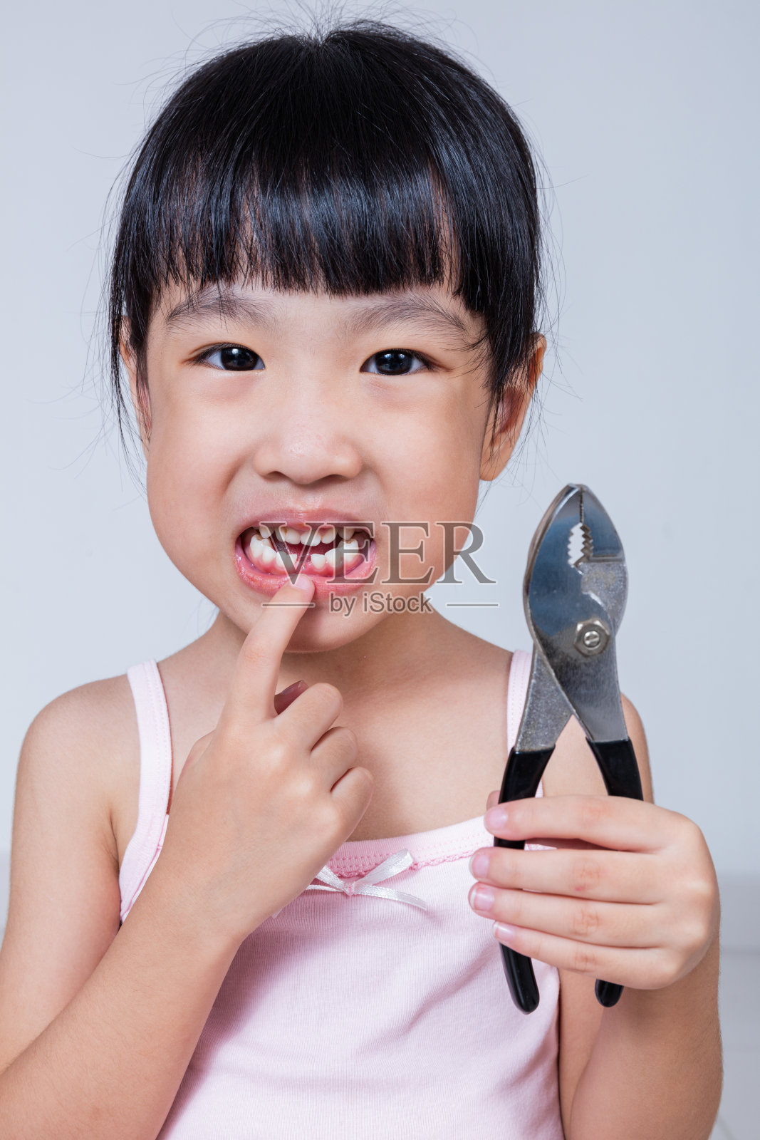 亚洲华人小女孩拿着钳子，露出缺口照片摄影图片