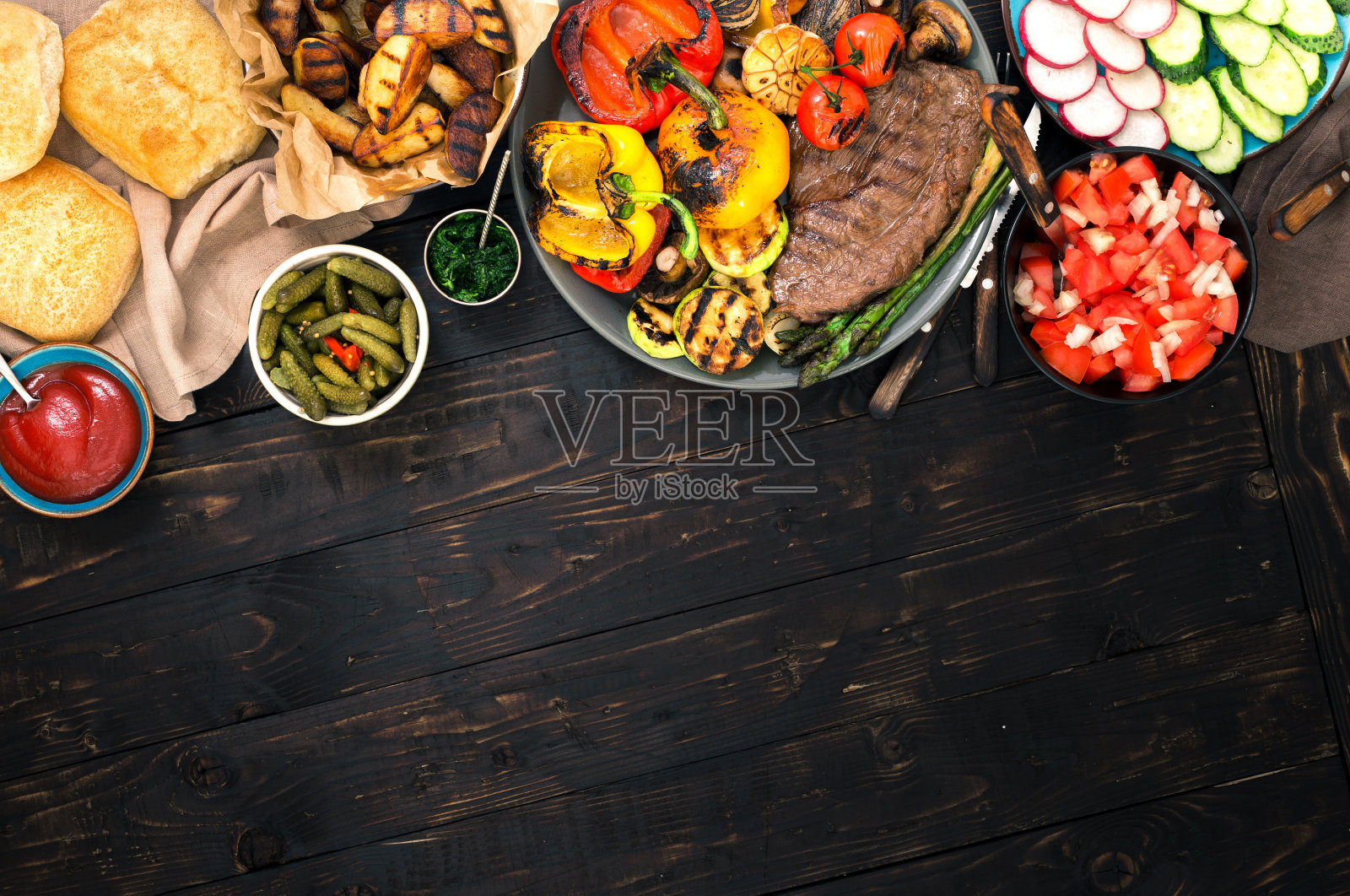 不同的食物在烤架上烹饪，烤牛排和烤蔬菜在有边框的木桌上照片摄影图片
