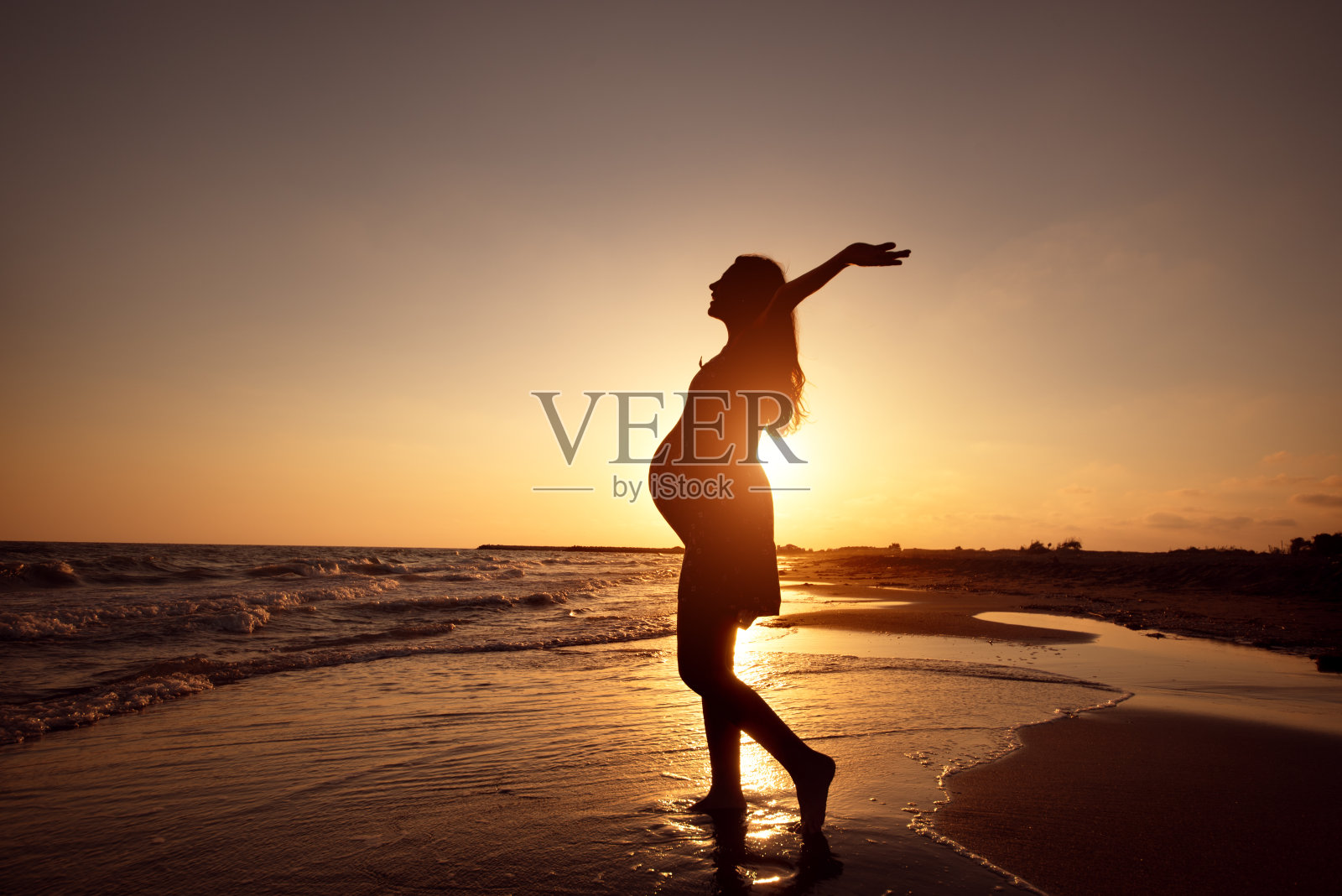 海滩上的孕妇的剪影在海上日落照片摄影图片