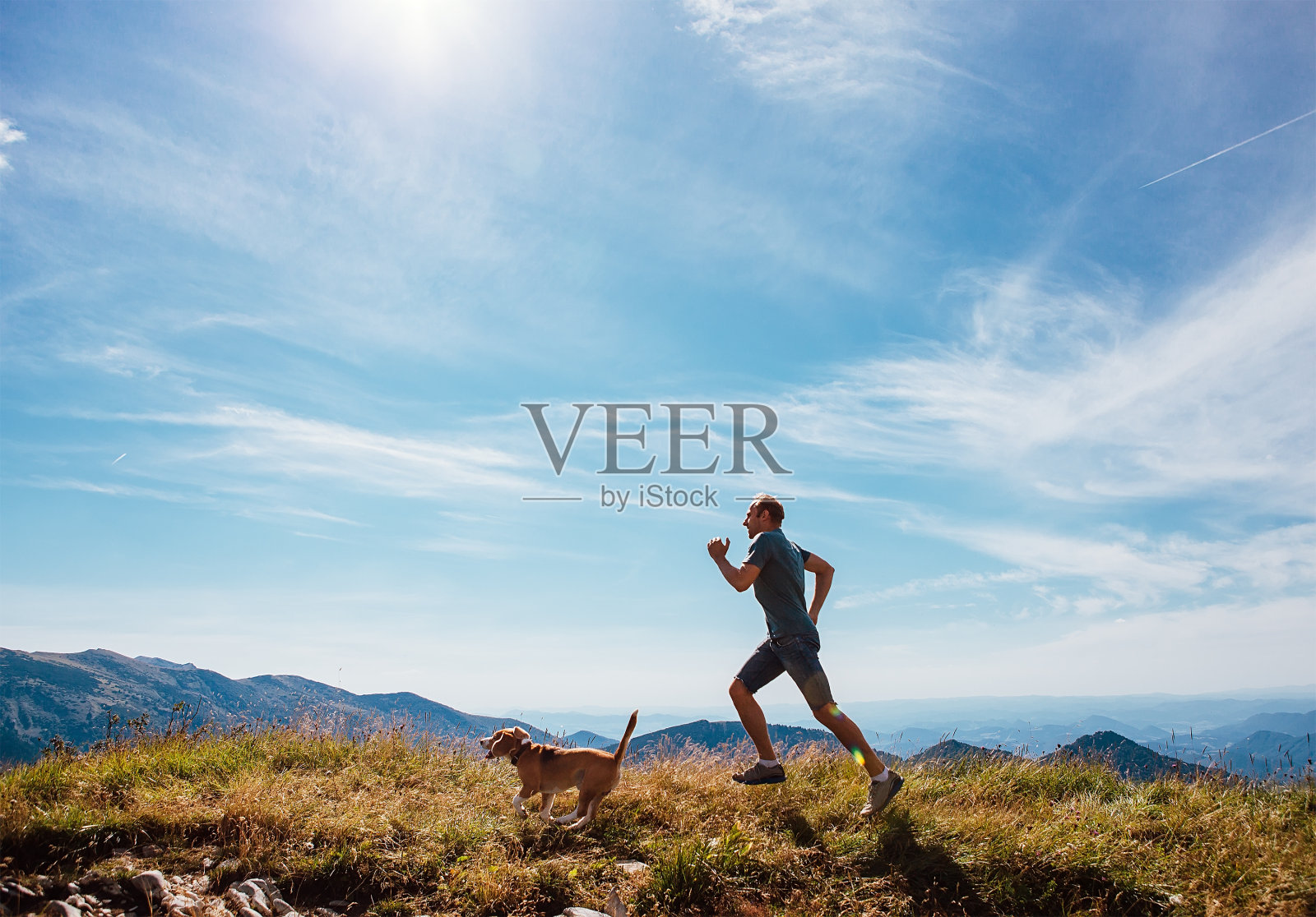 一个人和他的小猎犬在山顶上奔跑照片摄影图片