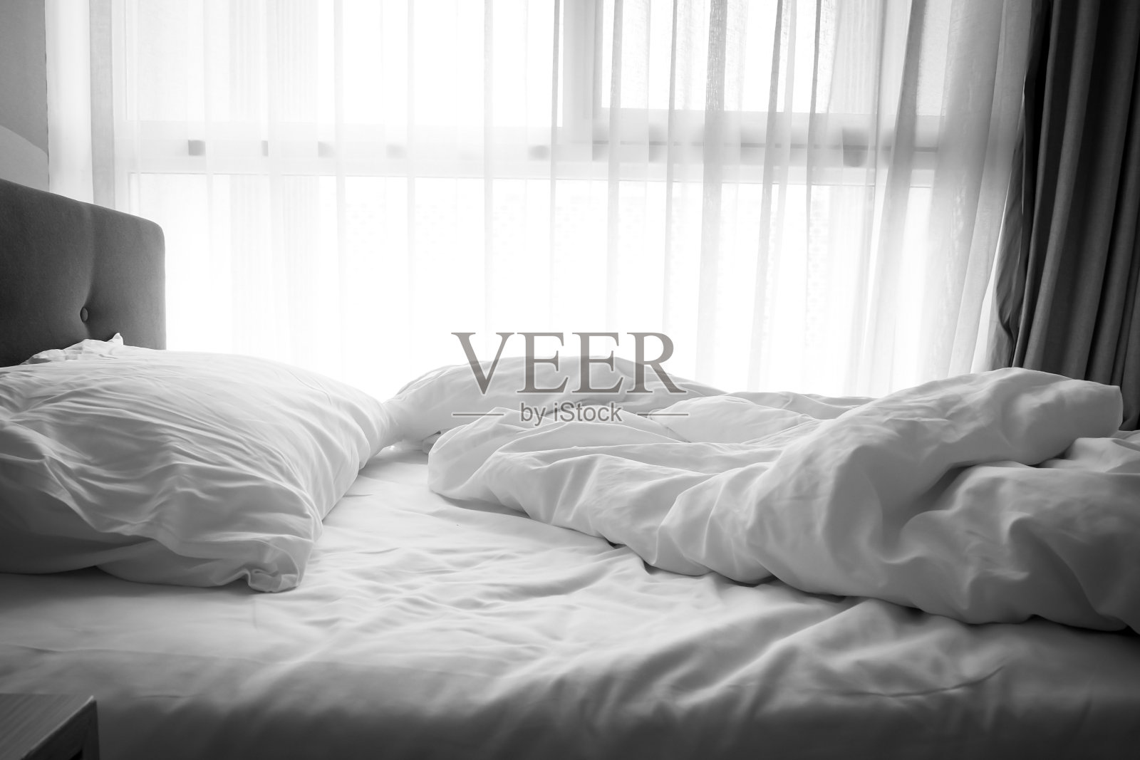 凌乱的床上。床上的白色枕头和毛毯未整理。早晨过后放松的概念。黑暗的小插图。照片摄影图片