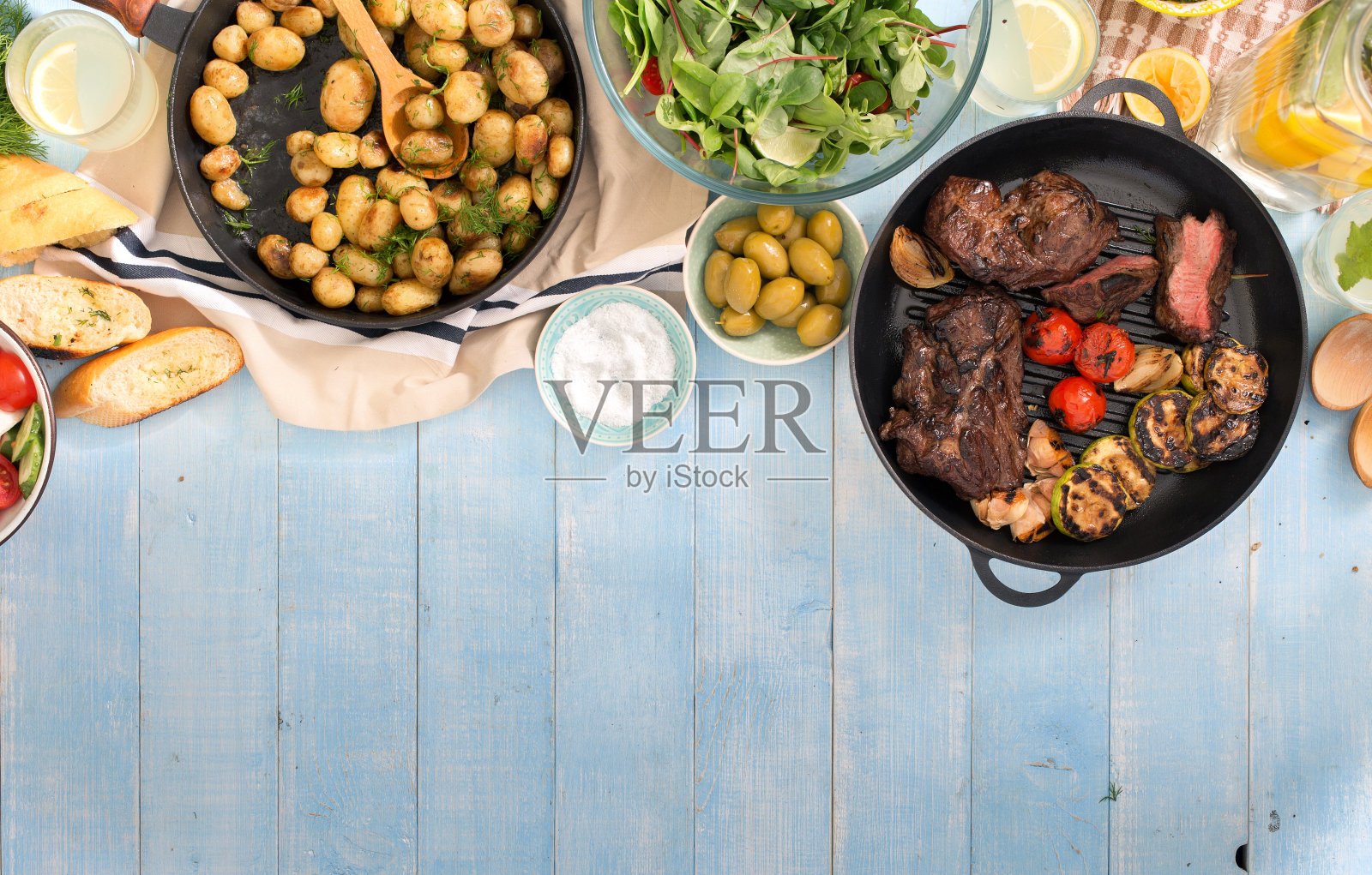 烤牛排、烤蔬菜、土豆、沙拉、各种小吃和自制柠檬水放在带边的蓝色乡村木桌上照片摄影图片