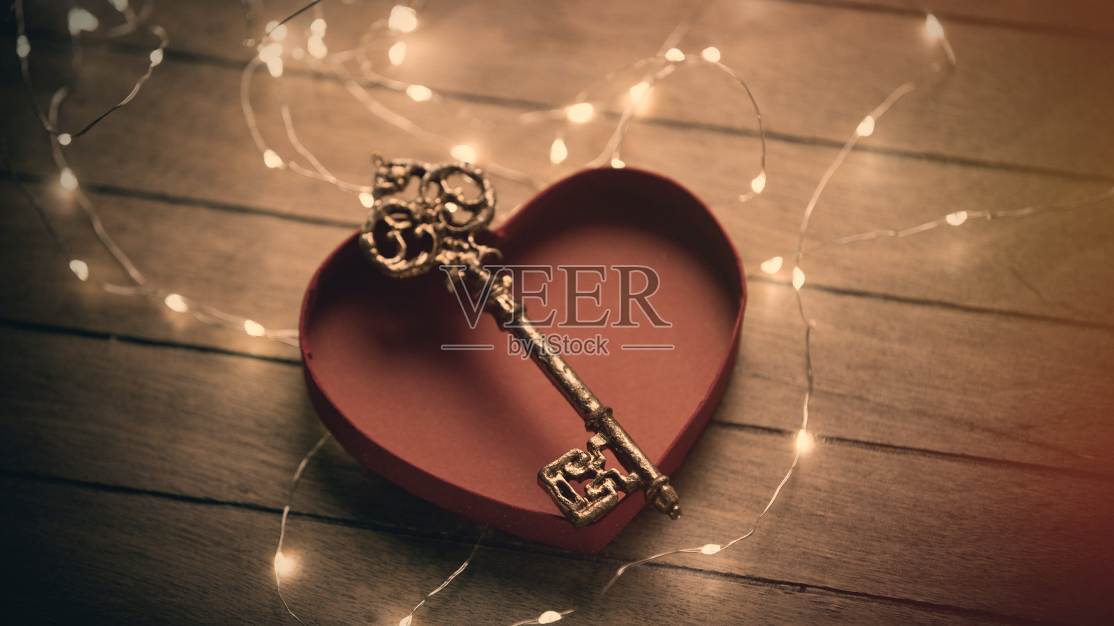 美丽的金钥匙在打开的心型盒子和花环在美妙的棕色背景照片摄影图片