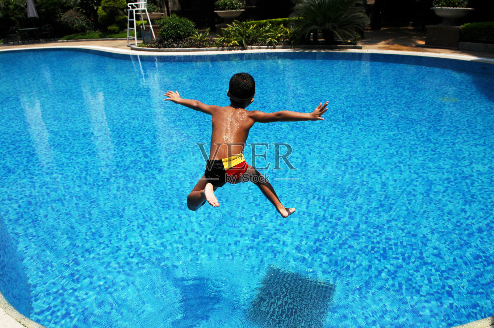 那个亚洲男孩跳进了蓝色的水里照片摄影图片
