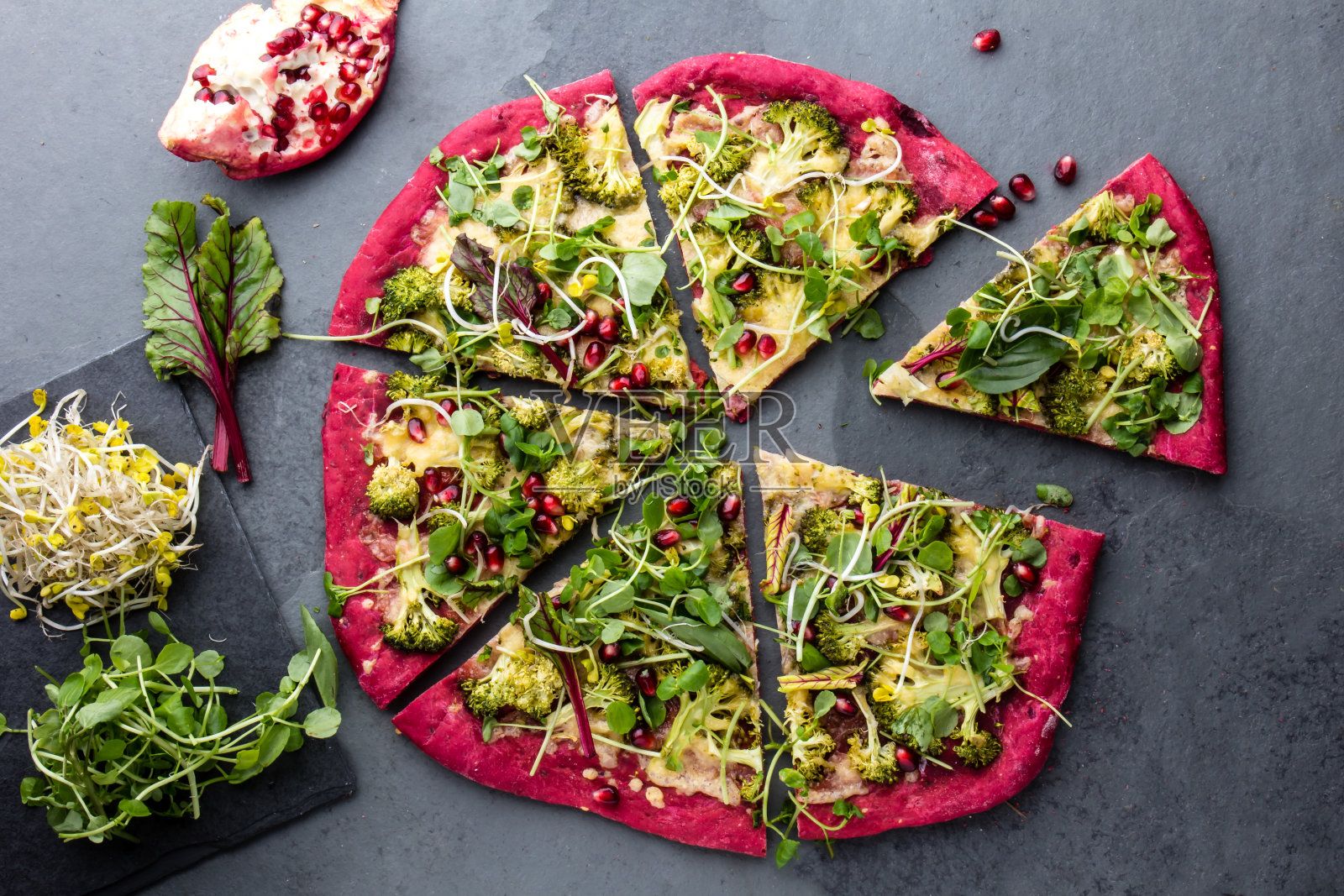 粉红色的甜菜根面团披萨与蔬菜，奶酪和新鲜的叶子和芽在灰色的石板背景。俯视图照片摄影图片