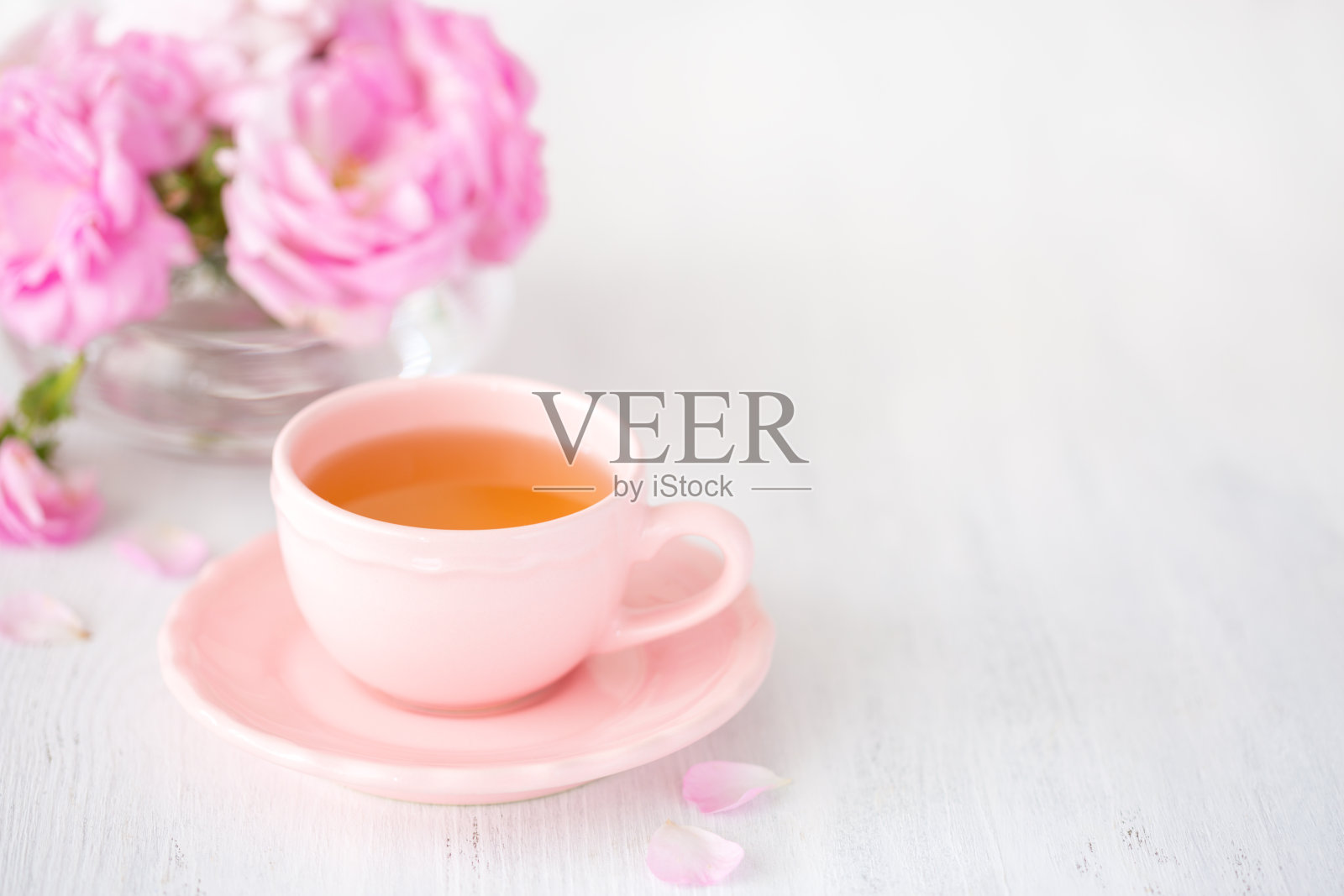 质朴的桌子上放着一杯茶和一束粉色玫瑰。照片摄影图片