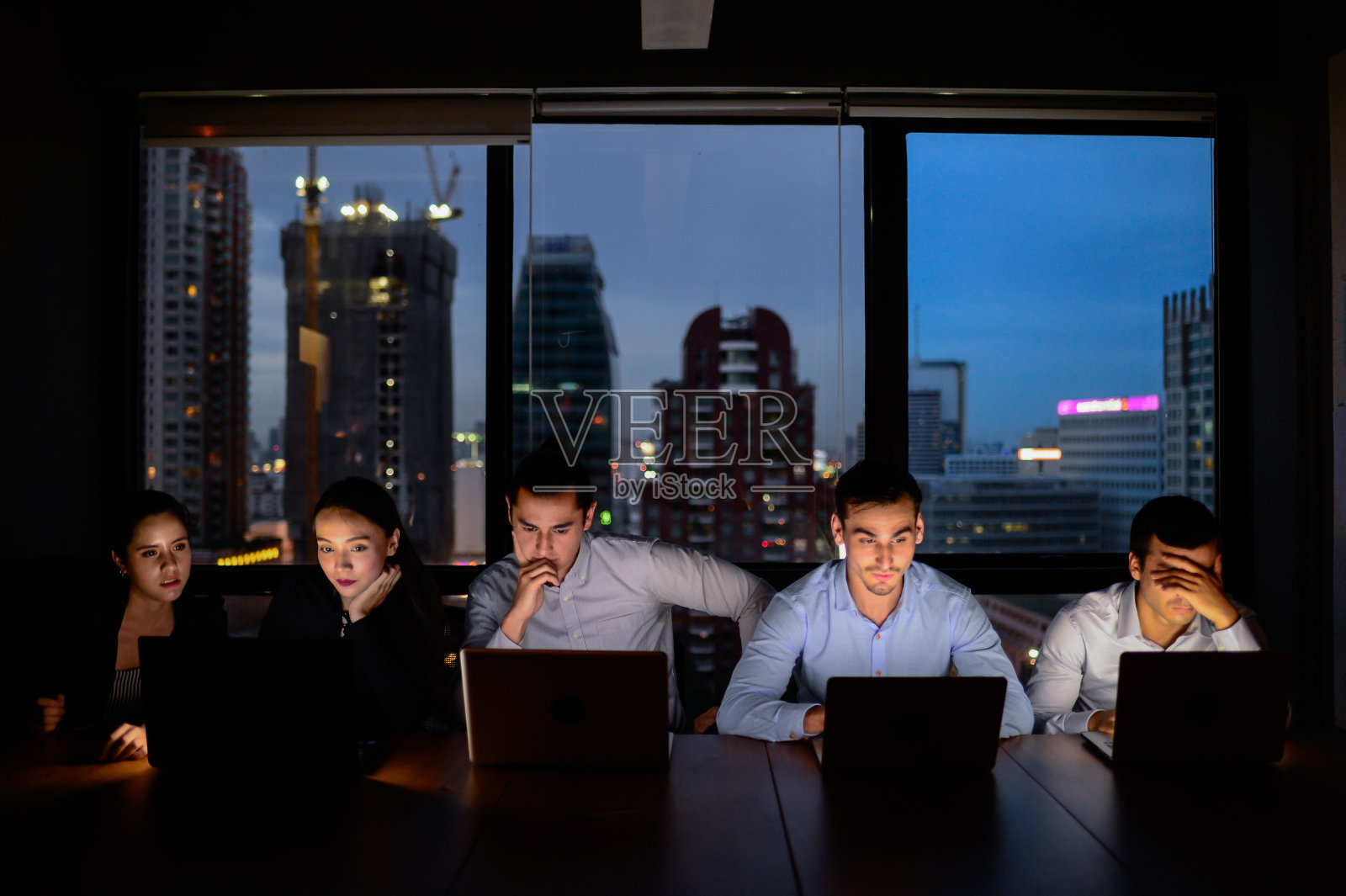 业务团队中，三男两女在夜晚和昏暗的灯光下加班用电脑工作照片摄影图片