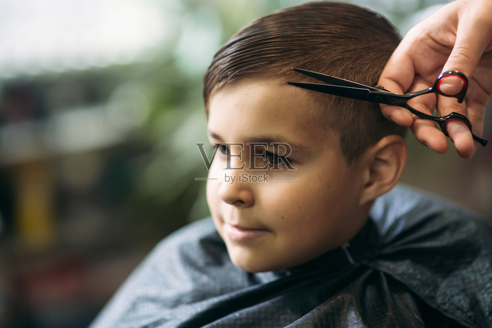 坐在理发店椅子上的小男孩正在理发。照片摄影图片
