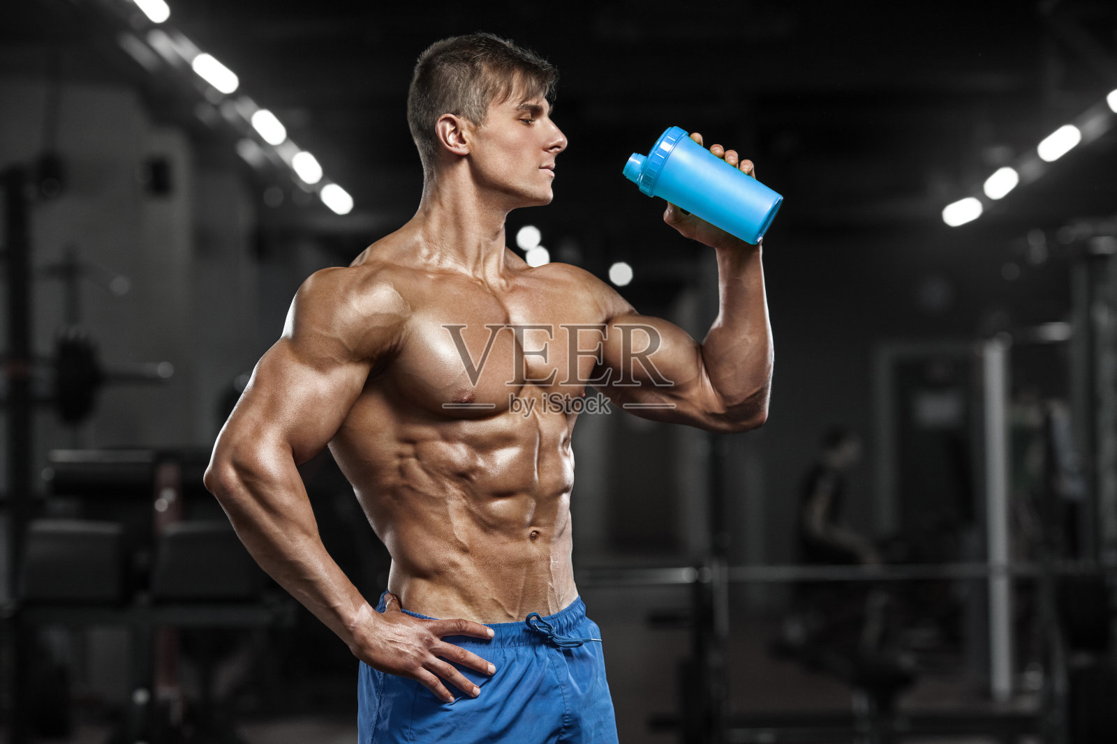 性感肌肉男在健身房喝水，塑形腹部。强壮的男性裸体躯干腹肌，锻炼照片摄影图片