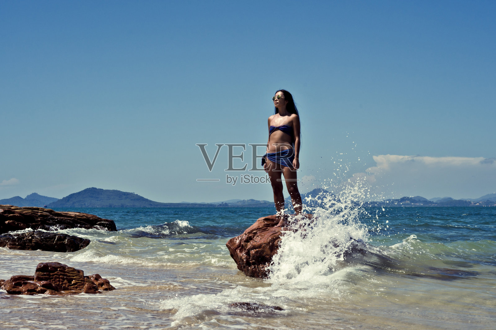 美丽的年轻亚洲女孩站在一块岩石在一个热带岛屿的冲浪线照片摄影图片