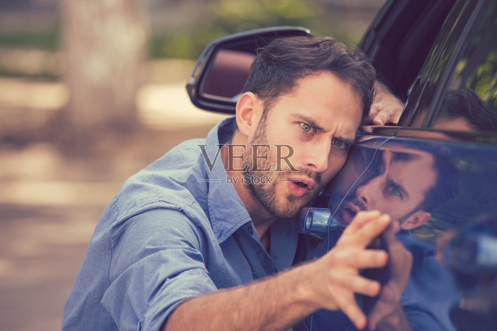 沮丧沮丧的年轻人看划痕和凹痕在他的汽车户外照片摄影图片