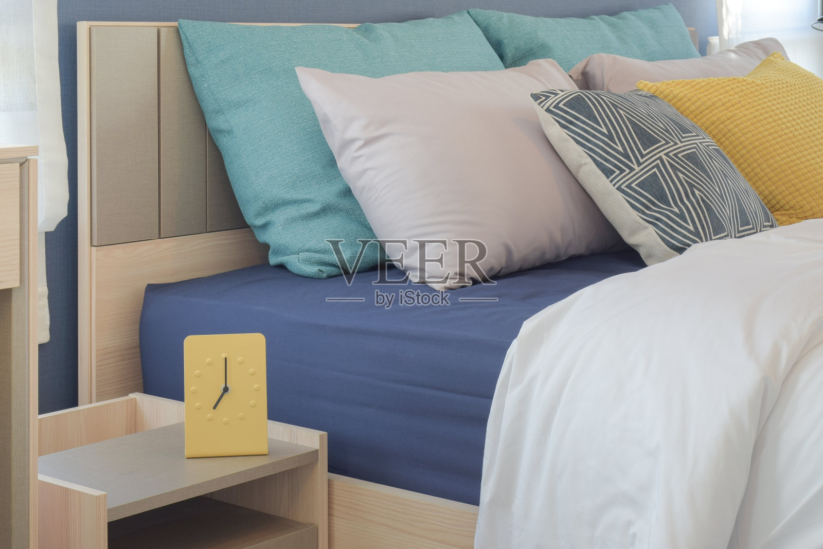 床上设有黄色和绿色的枕头，床边桌上有现代风格的黄色时钟照片摄影图片