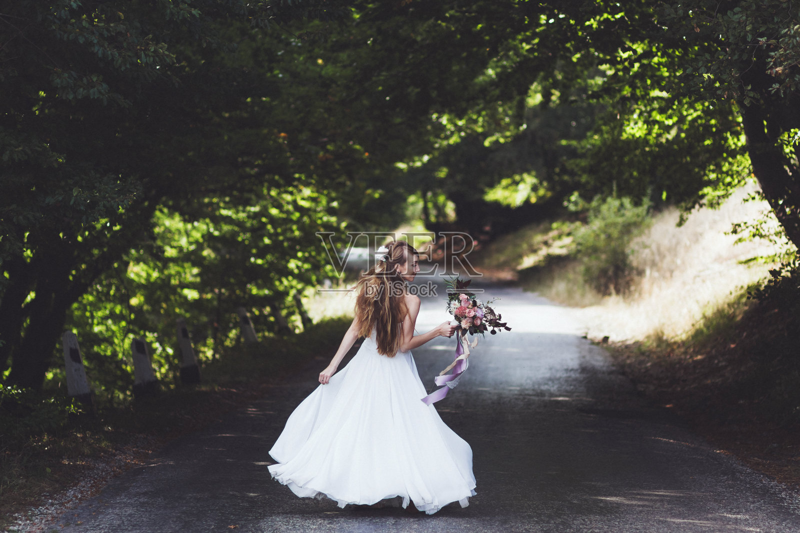 夏日乡村路上快乐新娘的肖像。带丝带的婚礼花束。她在舞蹈中旋转照片摄影图片