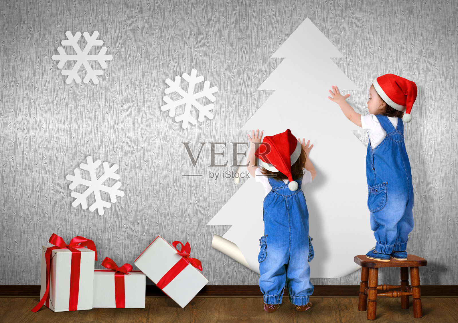 小双胞胎戴上圣诞帽，把圣诞树粘在家里的墙上，圣诞概念照片摄影图片