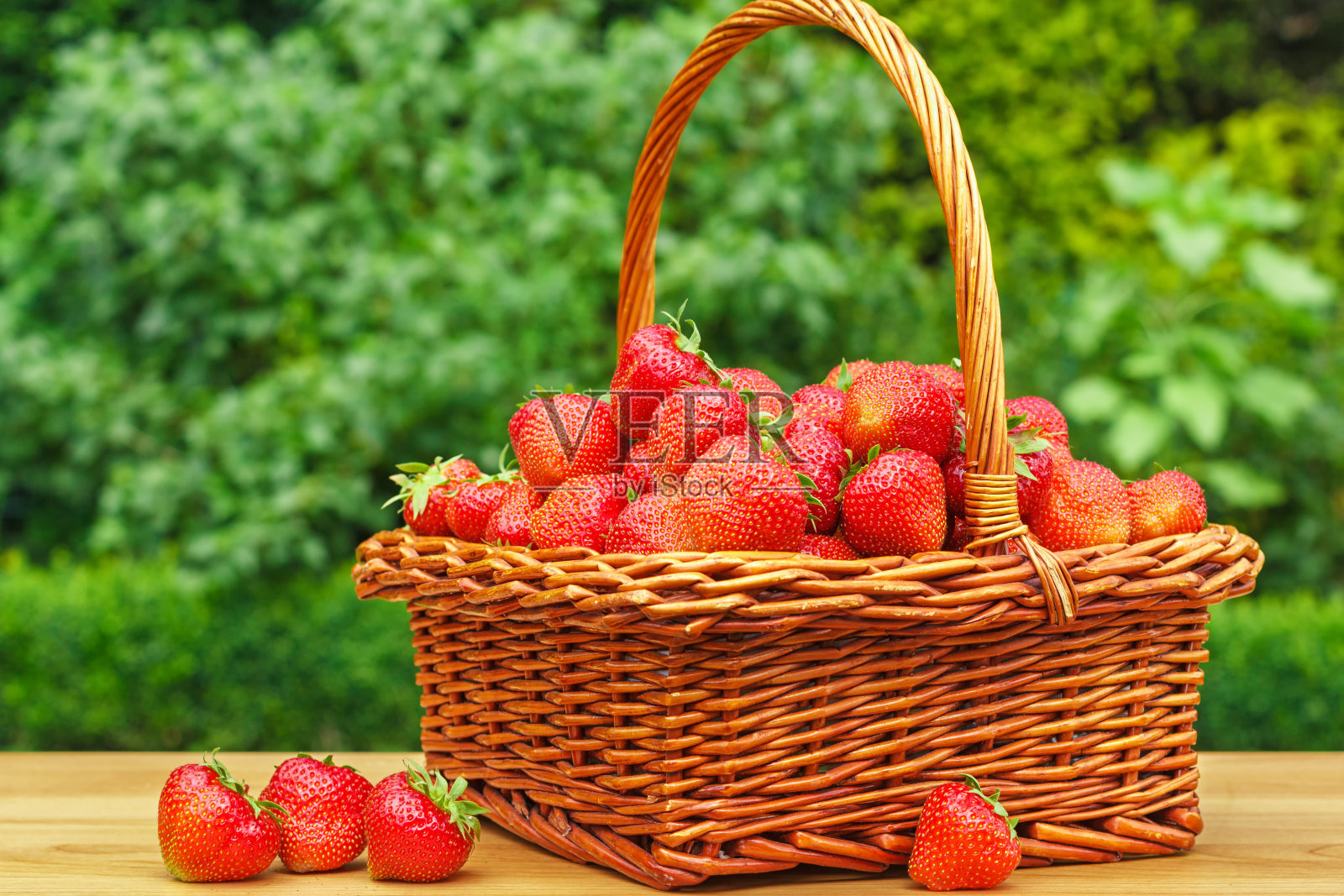 新鲜的草莓放在篮子里，放在花园里的木桌上照片摄影图片