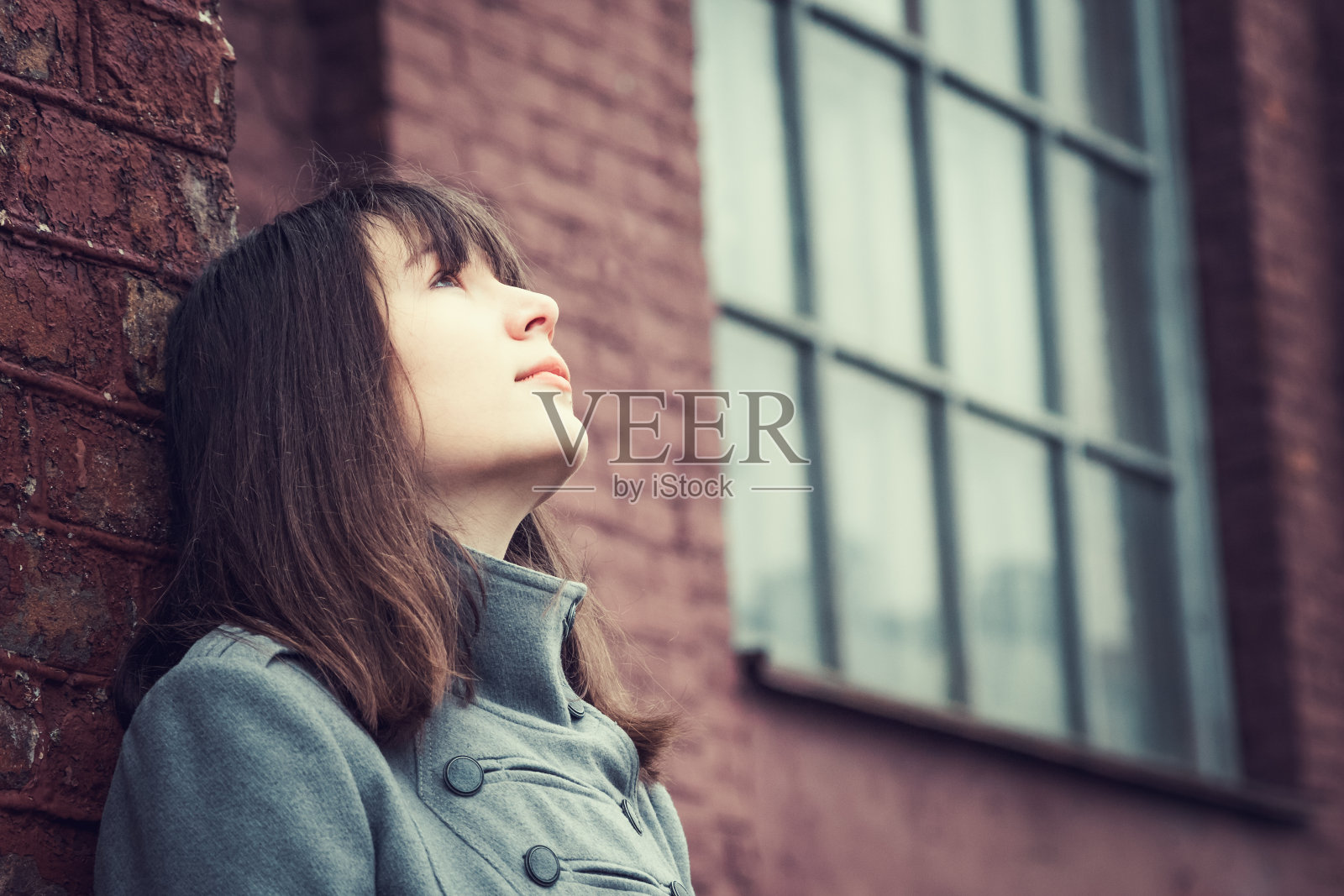 一个美丽的年轻姑娘站在砖墙旁边沉思着照片摄影图片