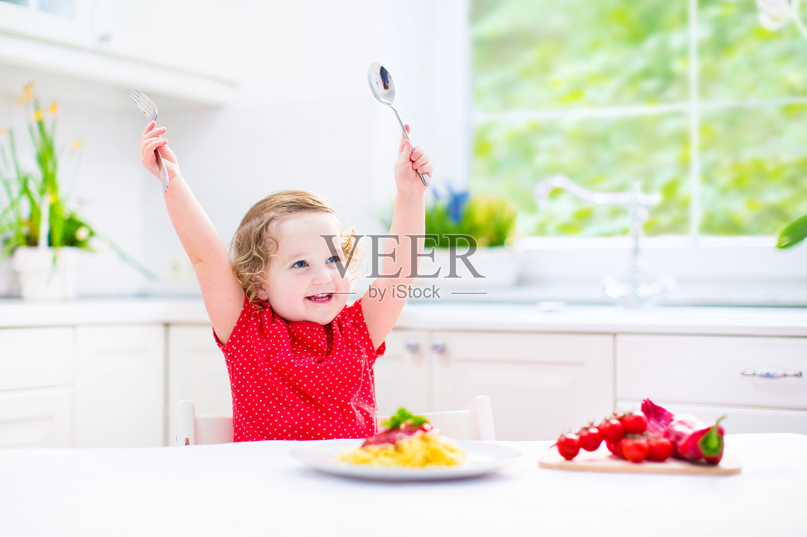 笑着蹒跚学步的小女孩玩着叉子和勺子吃意大利面照片摄影图片