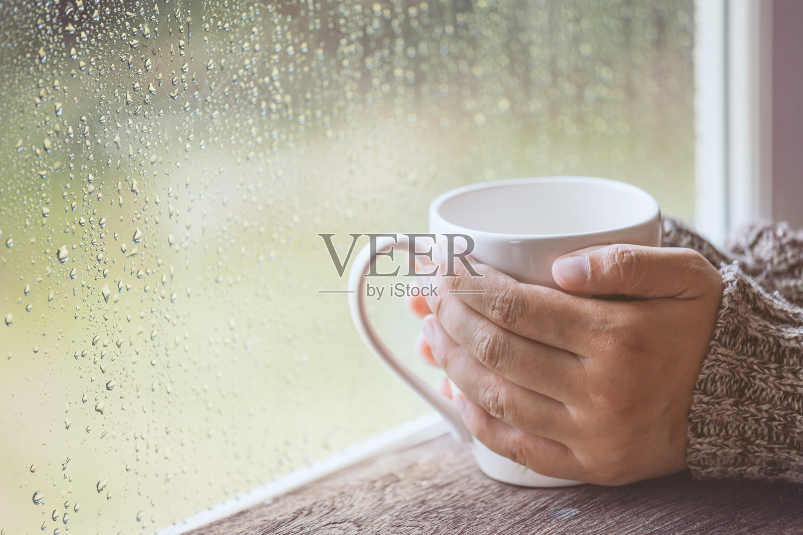 女人手拿着一杯咖啡或茶在雨天的窗户背景照片摄影图片