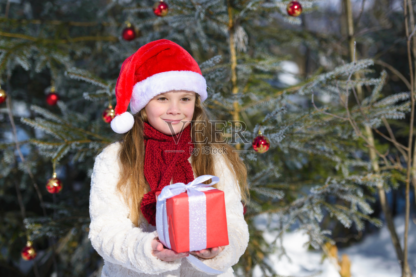 在冬天的森林里，微笑着的小女孩拿着圣诞礼物照片摄影图片