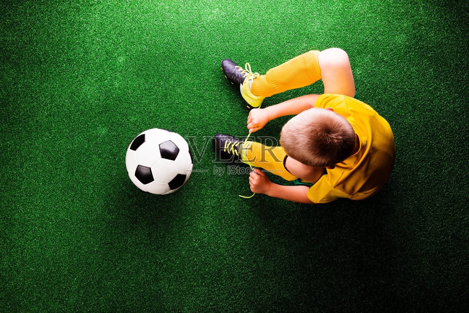 绿草如茵的草地上，一个面目全非的小足球运动员照片摄影图片