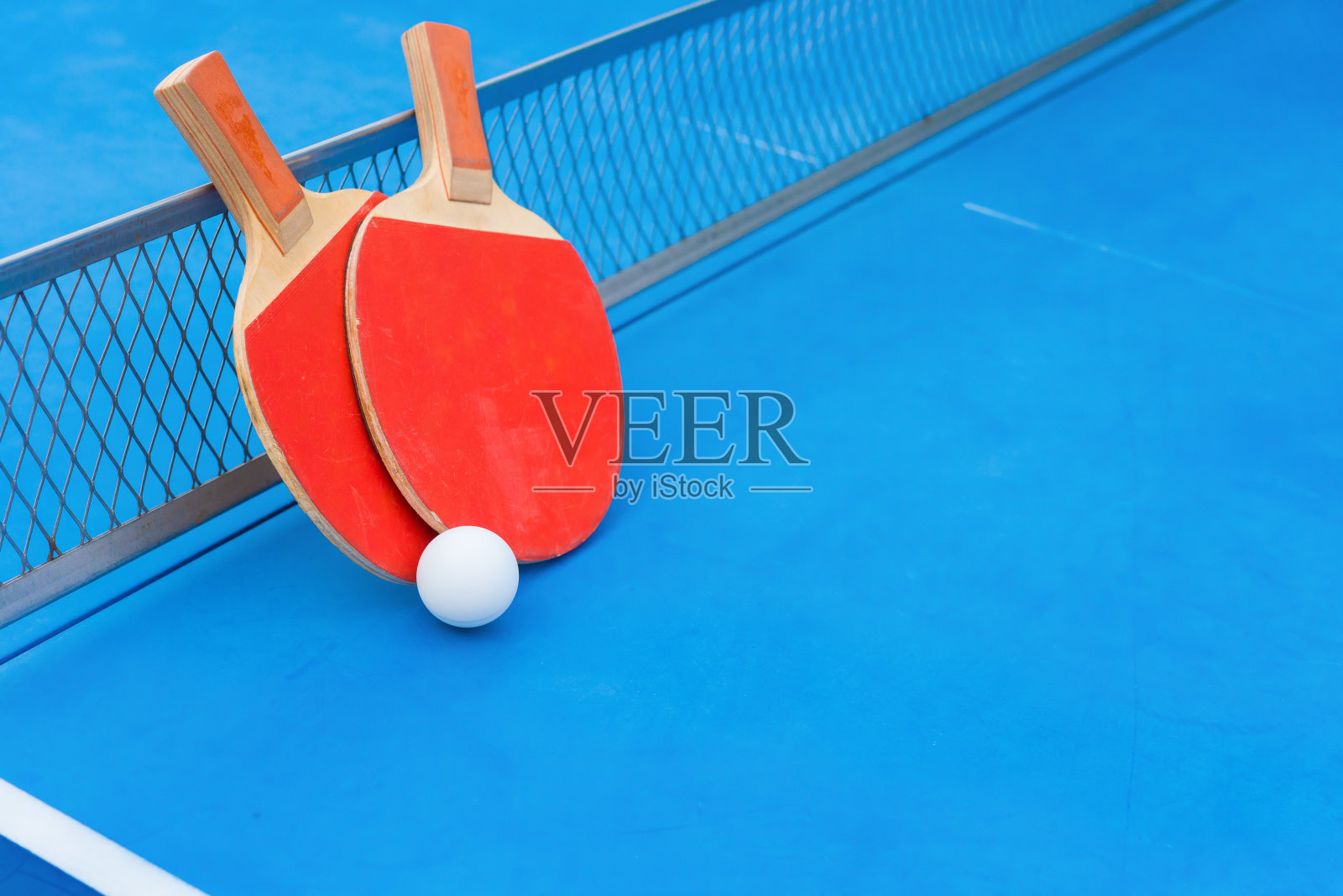 乒乓球拍、球和网放在蓝色的乒乓球桌上照片摄影图片