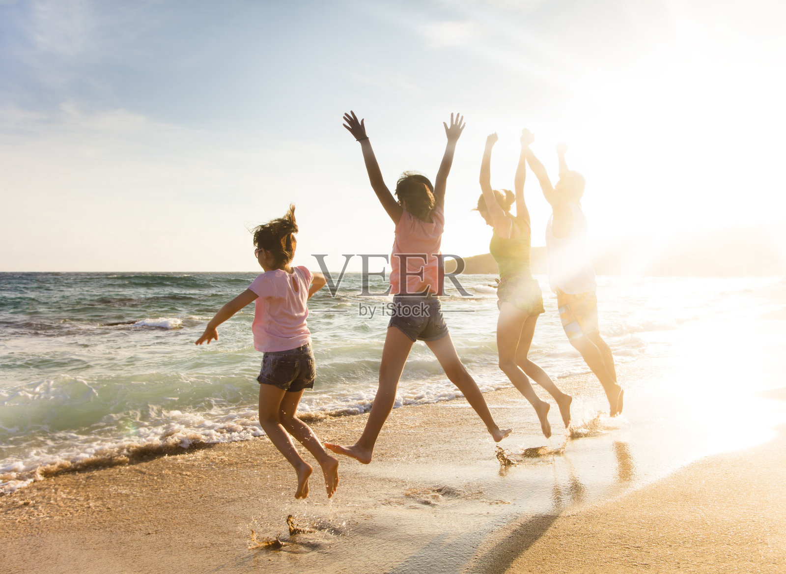 日落时分，快乐的小家庭在海滩上跳跃照片摄影图片