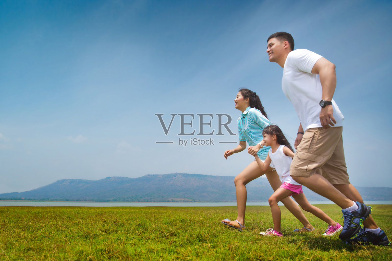 在开阔的草原上奔跑的亚洲家庭。照片摄影图片