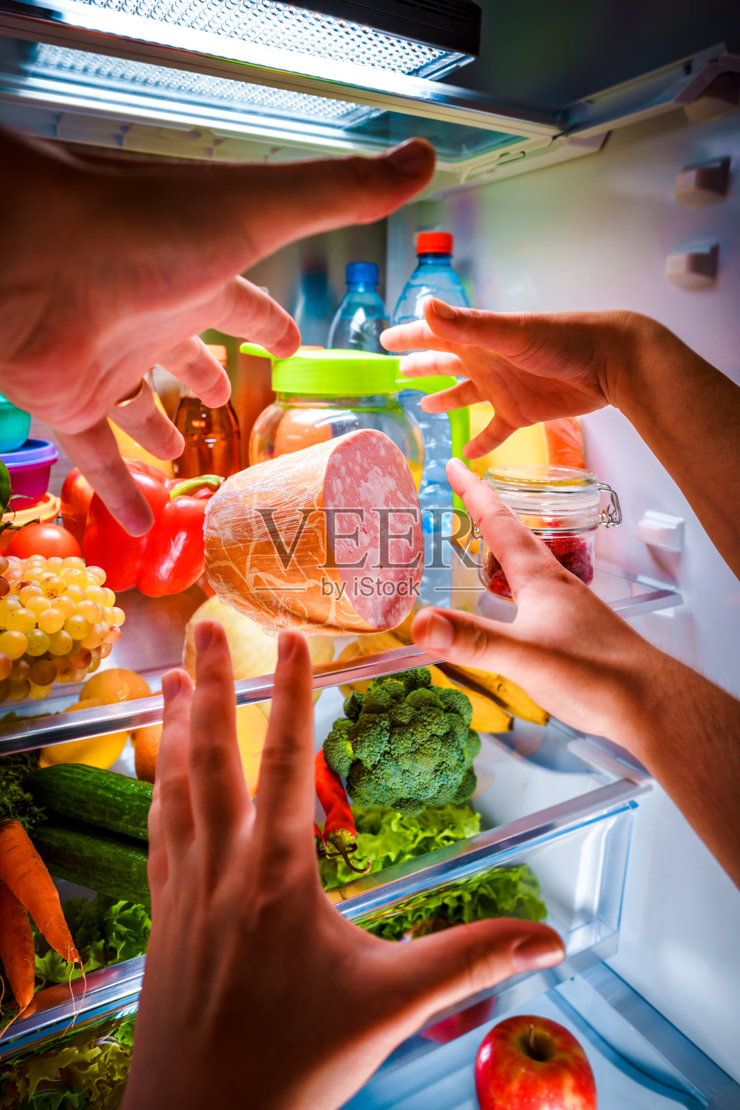 人们的手在晚上在打开的冰箱里拿食物照片摄影图片