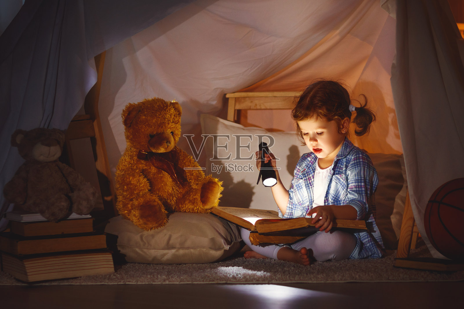 睡觉前拿着一本书、一个手电筒和泰迪熊的小女孩照片摄影图片