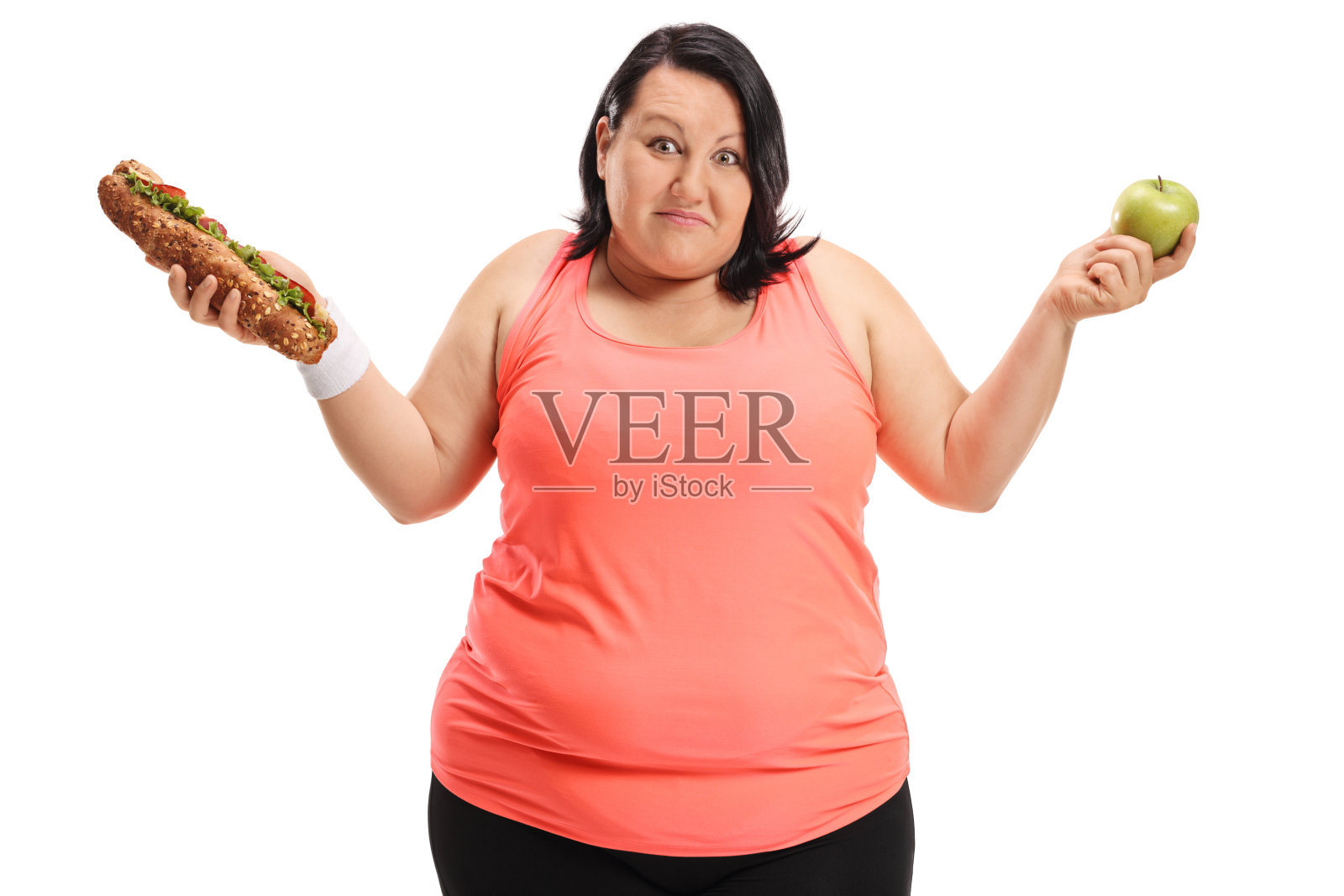 优柔寡断的超重女人拿着一个三明治和一个苹果照片摄影图片