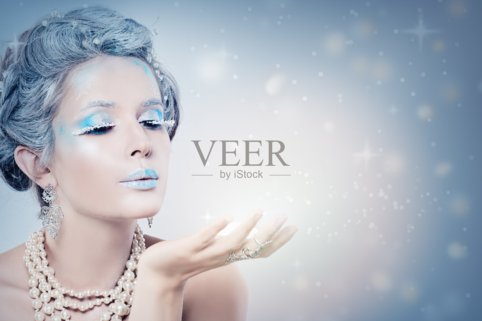冬天的女人时尚模特在晚上吹雪。白雪皇后女孩在蓝色背景与星星，雪和闪光照片摄影图片