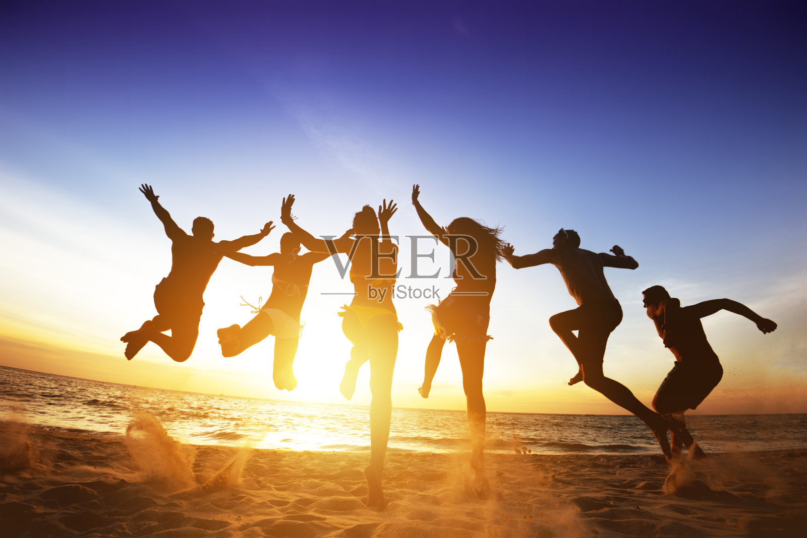 快乐的朋友跳跃海滩夕阳。友谊或团队概念照片摄影图片