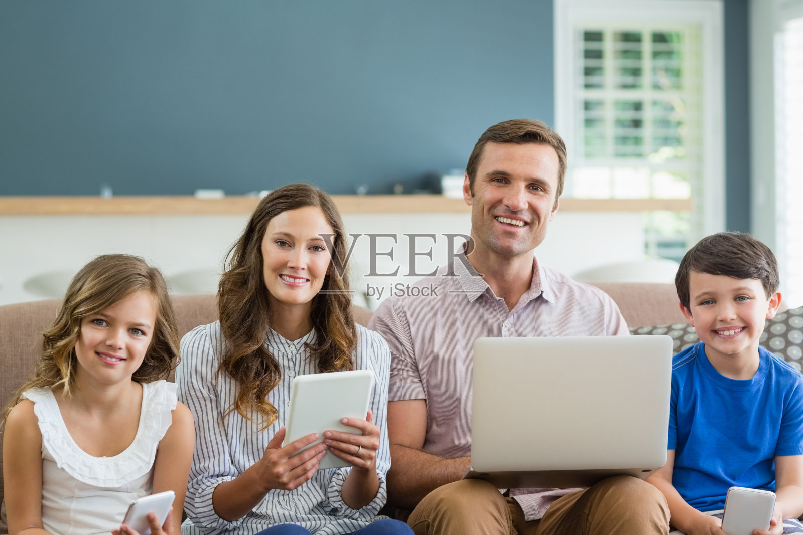 微笑的家庭使用数字平板电脑，手机和笔记本电脑在家里的客厅照片摄影图片