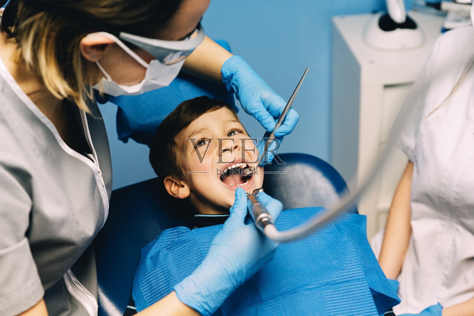 牙医在与病人进行牙科干预期间对男孩进行治疗。照片摄影图片