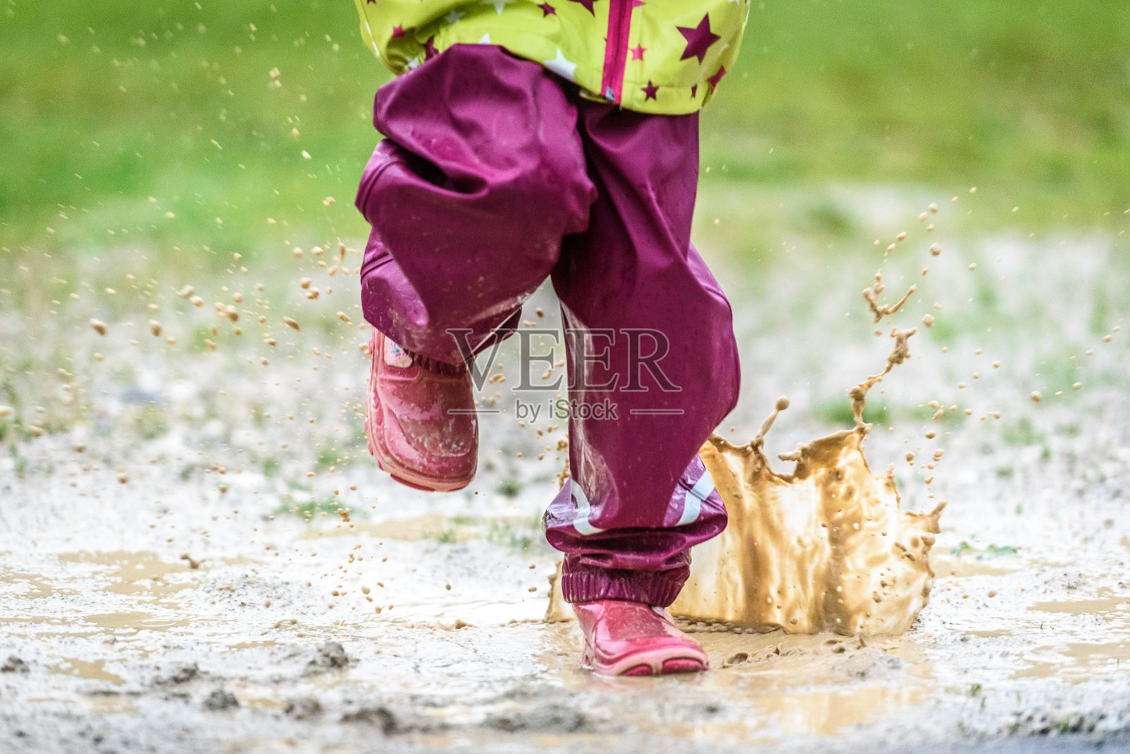 孩子们穿着胶靴和雨衣在水坑里跳来跳去。照片摄影图片