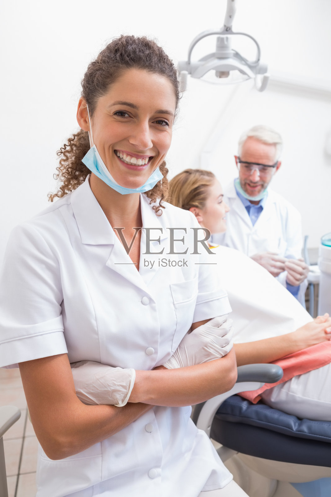 牙医助理对着镜头微笑，牙医和病人在后面照片摄影图片