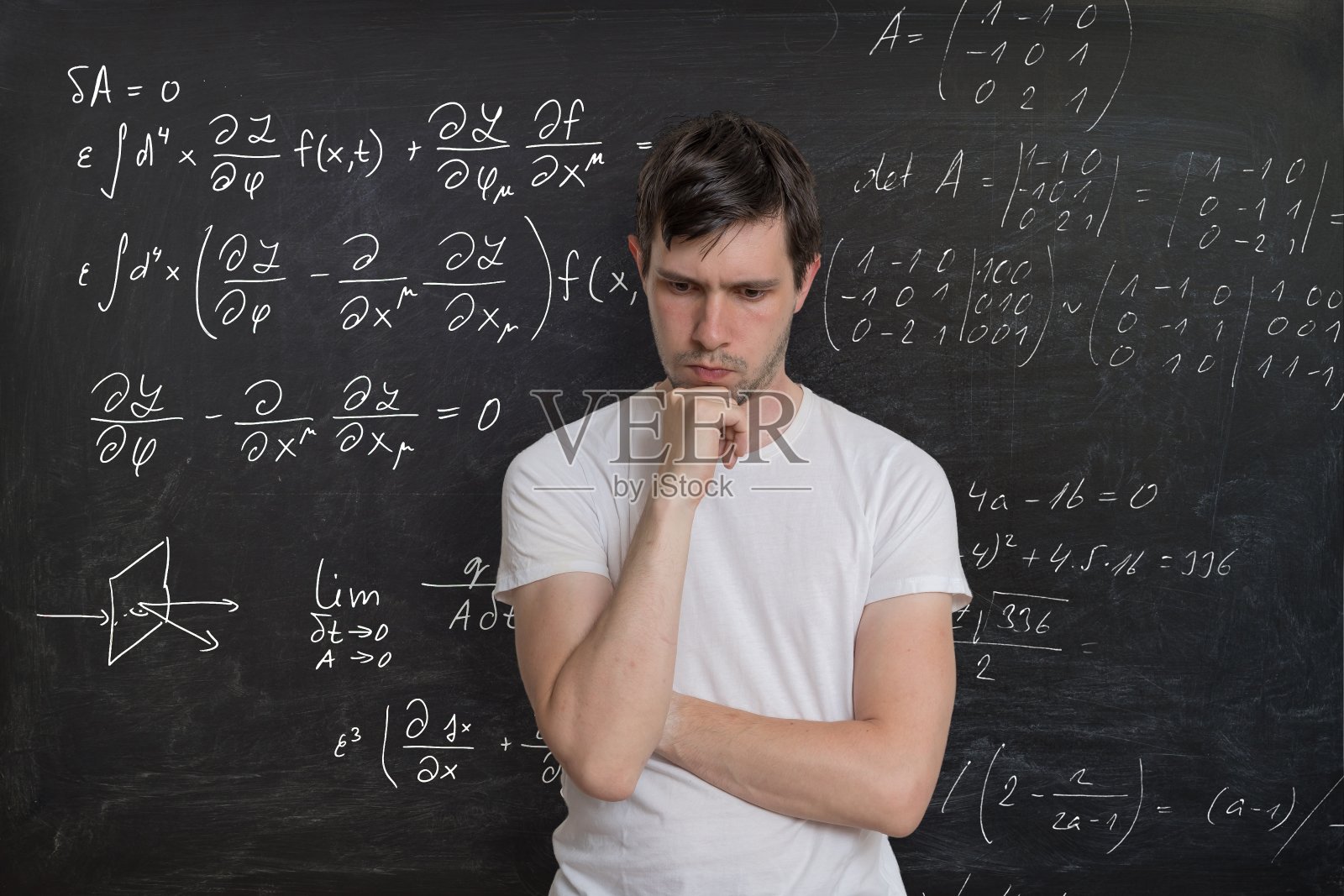 年轻的学生正在解决数学考试。背景黑板上的数学公式。照片摄影图片