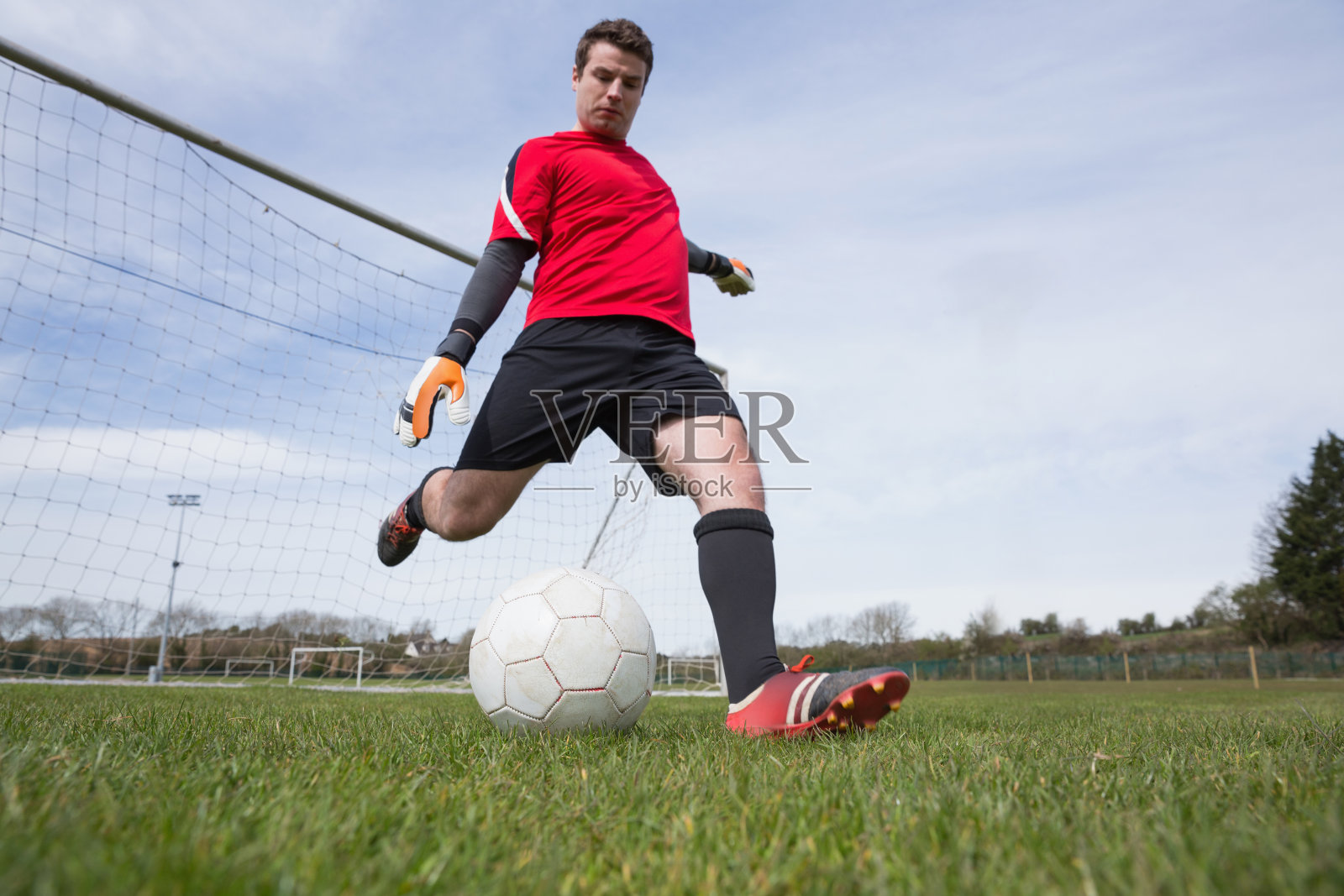 身着红色衣服的守门员将球踢出球门照片摄影图片