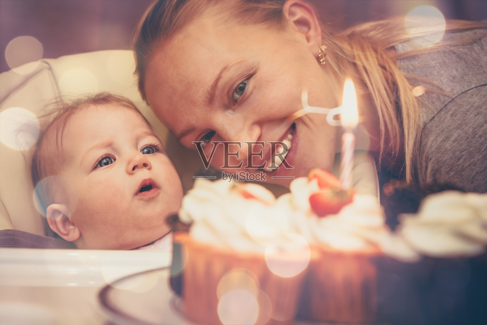 在庆祝宝宝的第一个生日时，妈妈用蜡烛看着生日蛋糕照片摄影图片