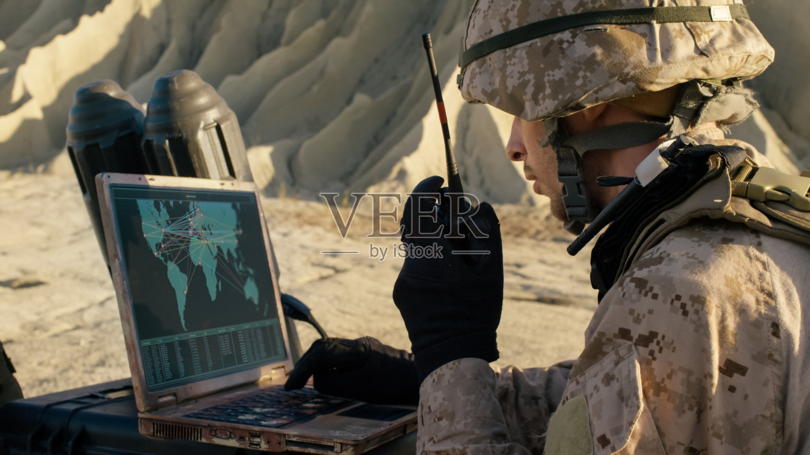 一名士兵在沙漠军事行动中使用笔记本电脑和无线电进行通信。照片摄影图片