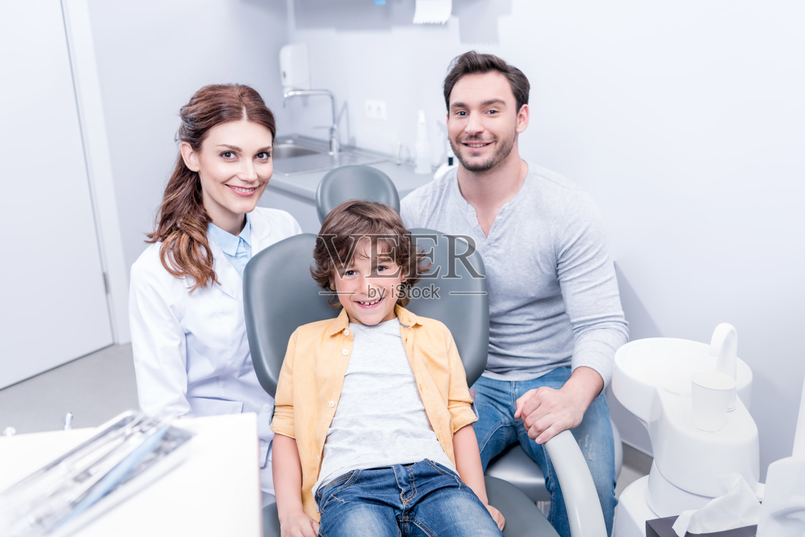微笑的小男孩与父亲和牙医在牙医诊所照片摄影图片